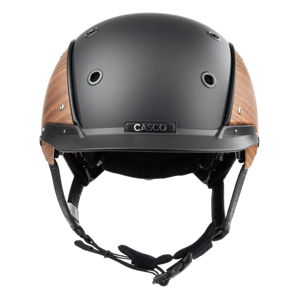 A matte black equestrian riding Casco helmet with natural wood-look panels on the sides, featuring a black chin strap and a visible 'CASCO' brand plate on the front.