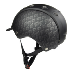 A black equestrian CASCO helmet featuring a subtle repeating circular logo pattern on the front shell, with matte black plastic trim and adjustable black chin straps.