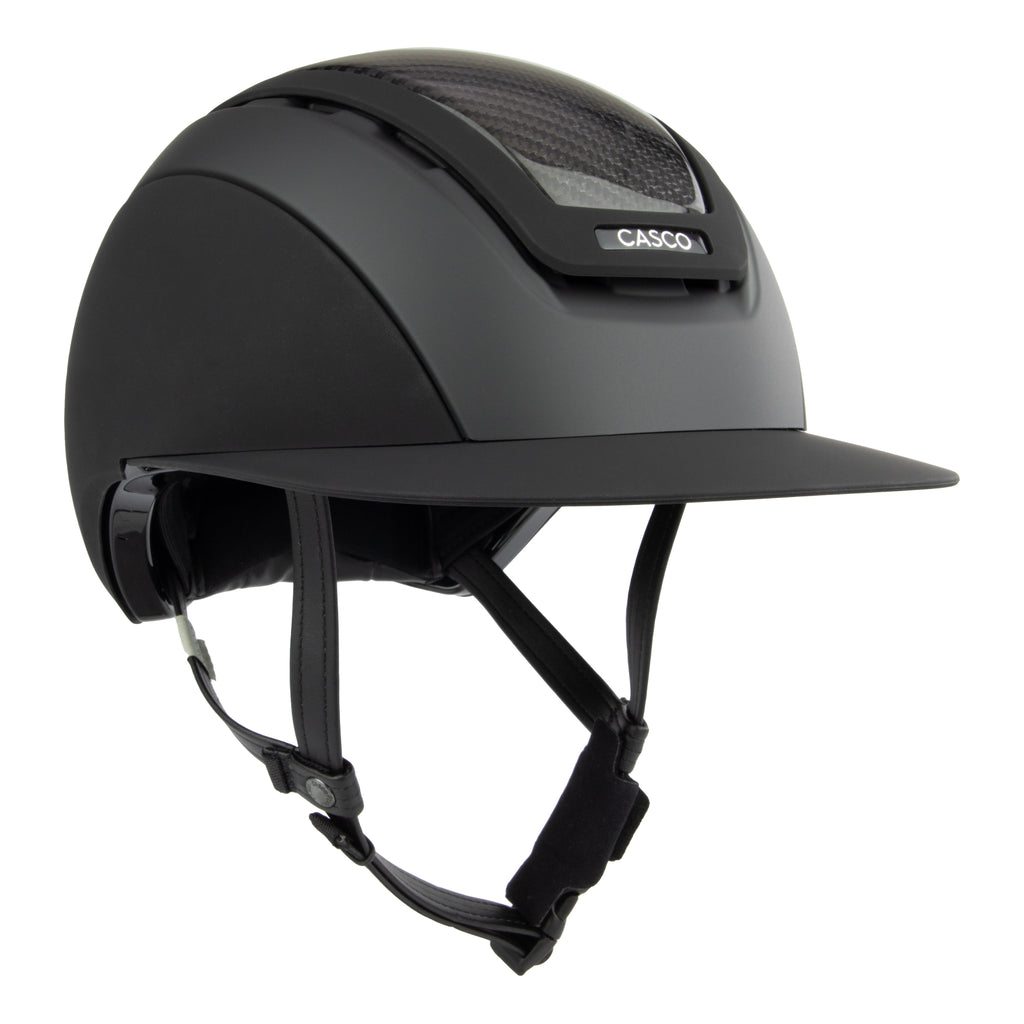 A matte black equestrian riding Casco helmet with a visor and chin straps, featuring a carbon-fiber patterned ventilation window and a visible CASCO brand badge.