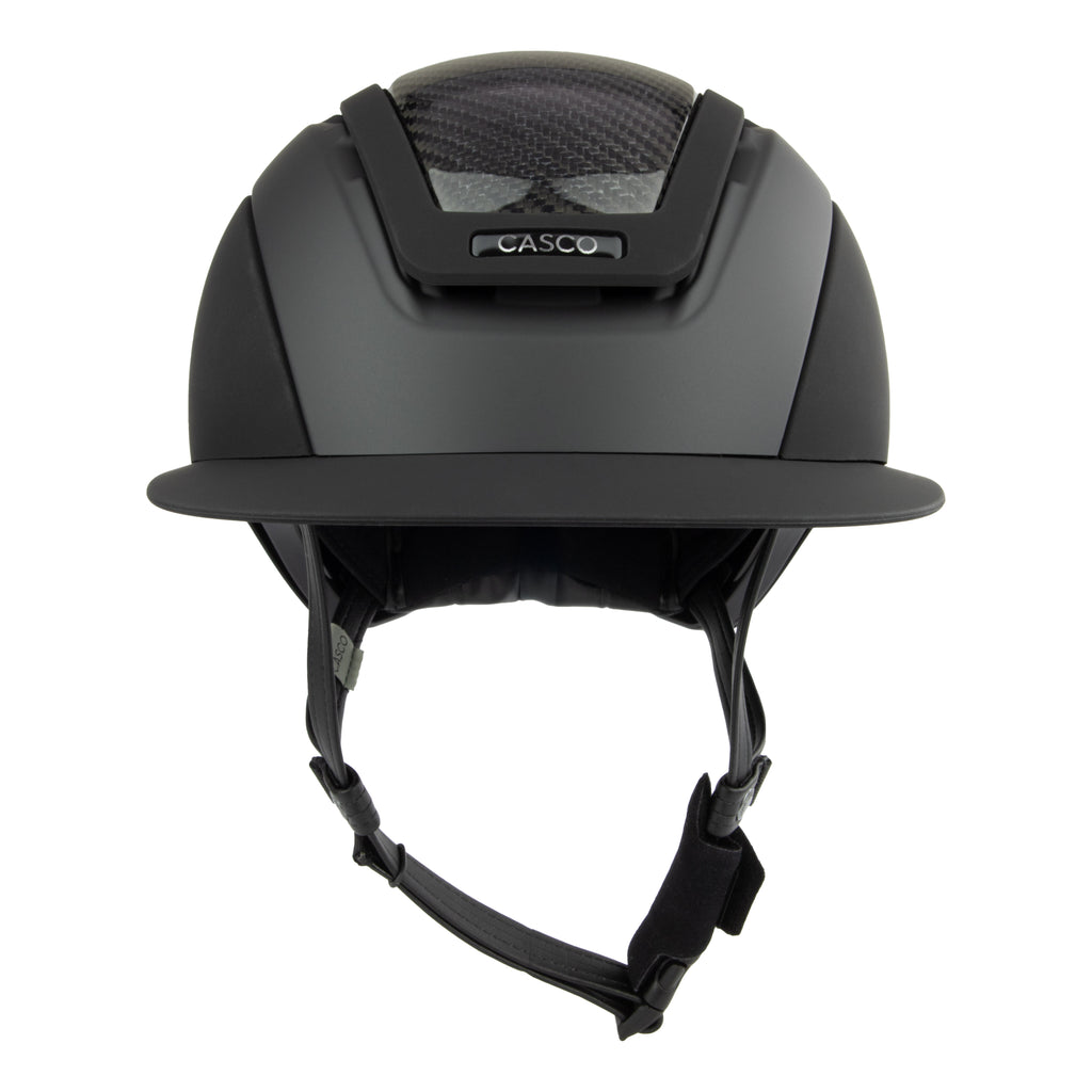 A matte black Casco equestrian helmet with a visor, black chin strap, and a textured carbon-fiber pattern on the top front, shown against a plain white background.