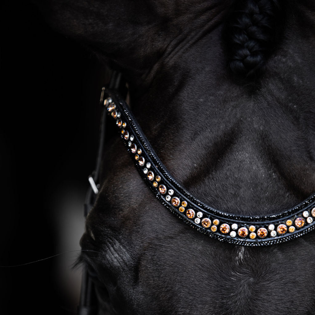 Closeup horse head wearing of the Lumiere Ariana browband featuring a wide deep-drop crystal design — gold-toned Austrian stellux crystals framed by black crystals - Patent leather loops